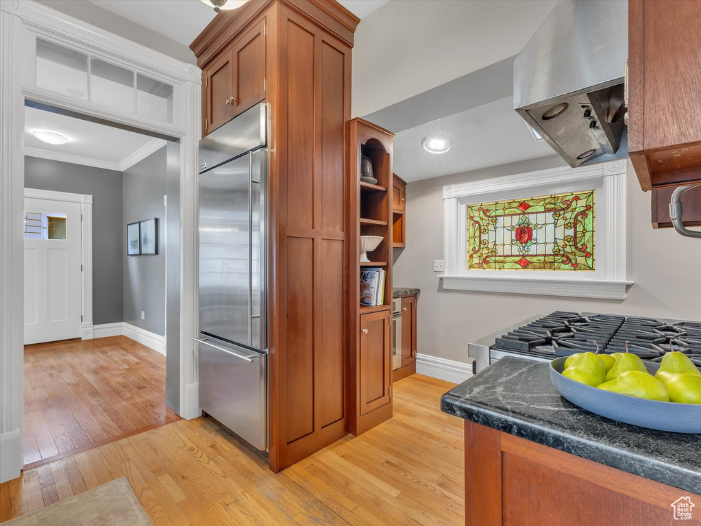 Kitchen featuring built in fridge, extractor fan, brown cabinets, light wood-style flooring, and ornamental molding