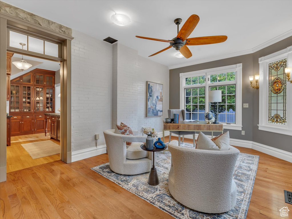 Living room featuring wood finished floors, ceiling fan, brick wall, baseboards, and a desk