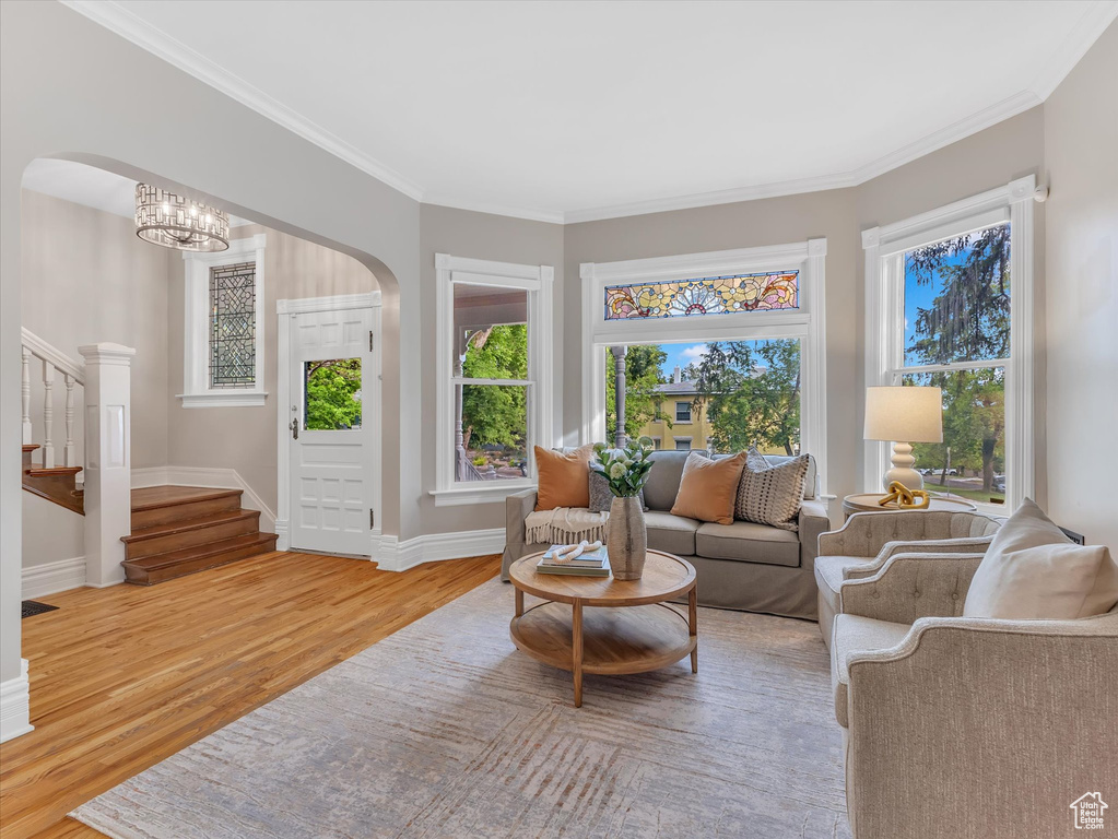 Living area with arched walkways, stairway, light wood finished floors, baseboards, and crown molding