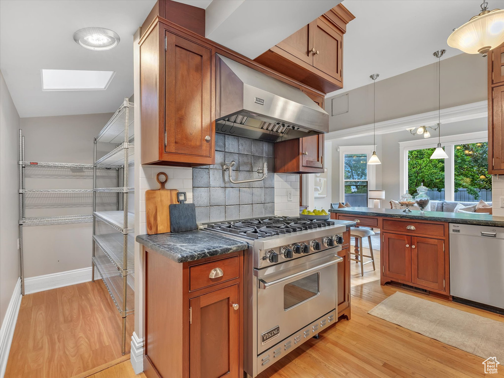 Kitchen featuring stainless steel appliances, under cabinet range hood, light wood-style floors, and tasteful backsplash