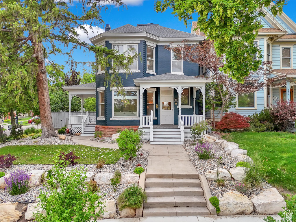 View of front facade featuring covered porch, stairs, a chimney, and a front yard