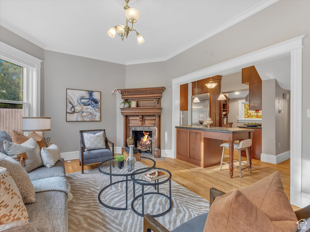 Living room featuring light wood-style floors, a premium fireplace, baseboards, ornamental molding, and a chandelier
