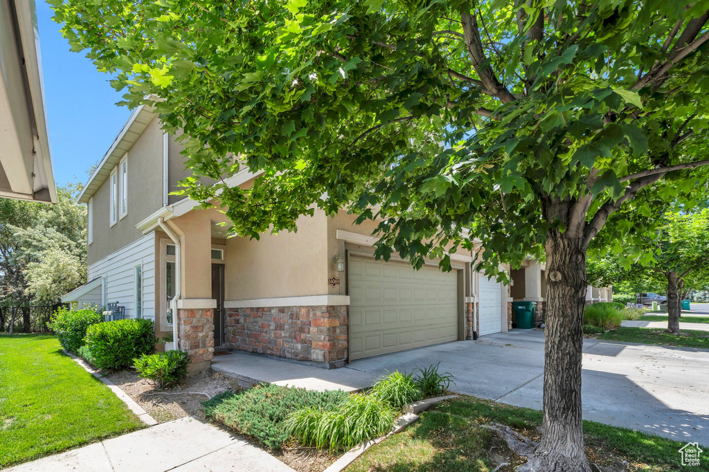 View of property hidden behind natural elements with stone siding, driveway, an attached garage, and stucco siding