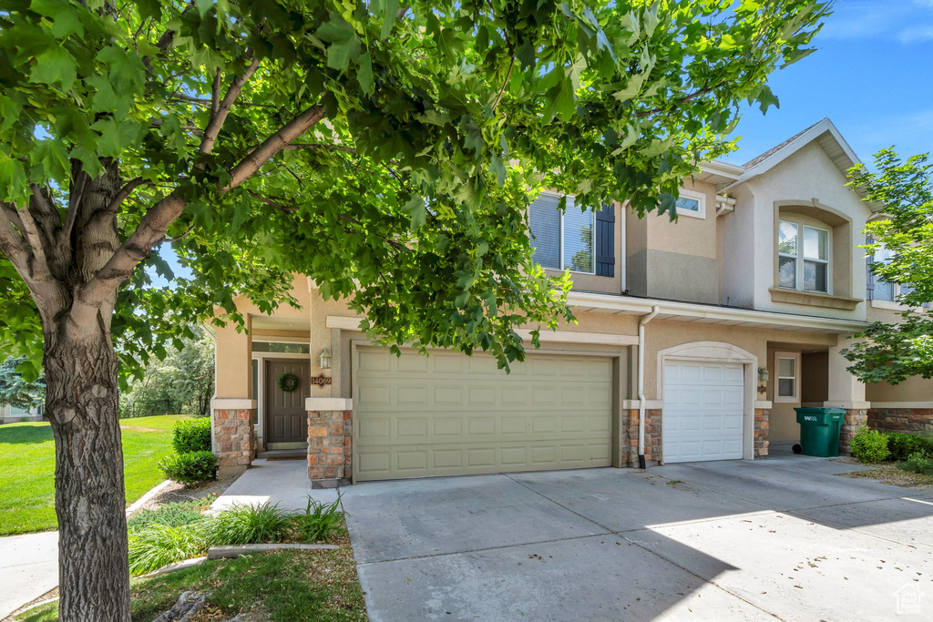 View of front of property featuring stone siding, an attached garage, concrete driveway, and stucco siding