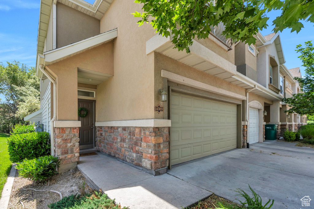 View of front of home featuring stucco siding, an attached garage, and stone siding