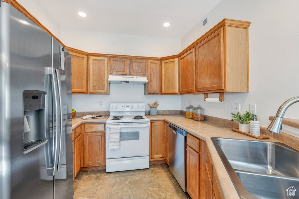 Kitchen featuring stainless steel appliances, a sink, under cabinet range hood, light countertops, and recessed lighting