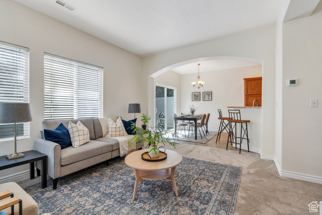 Living room featuring arched walkways, a chandelier, carpet, and baseboards