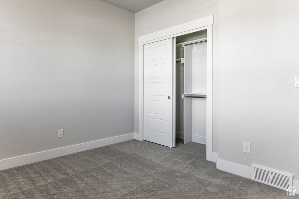 Unfurnished bedroom featuring dark carpet, baseboards, and a closet
