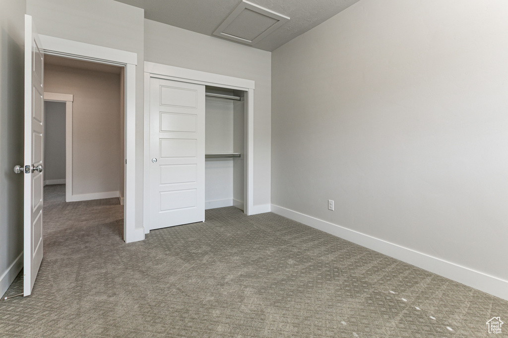 Unfurnished bedroom featuring attic access, carpet, baseboards, and a closet