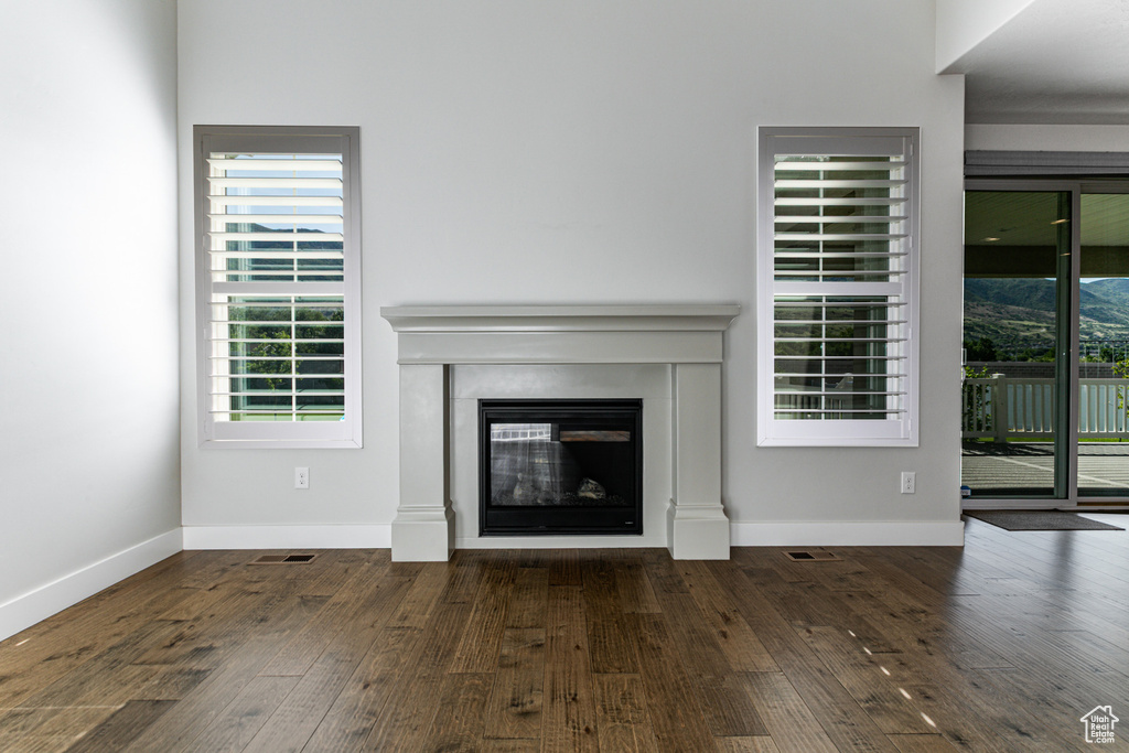 Unfurnished living room featuring hardwood / wood-style flooring, a glass covered fireplace, and baseboards