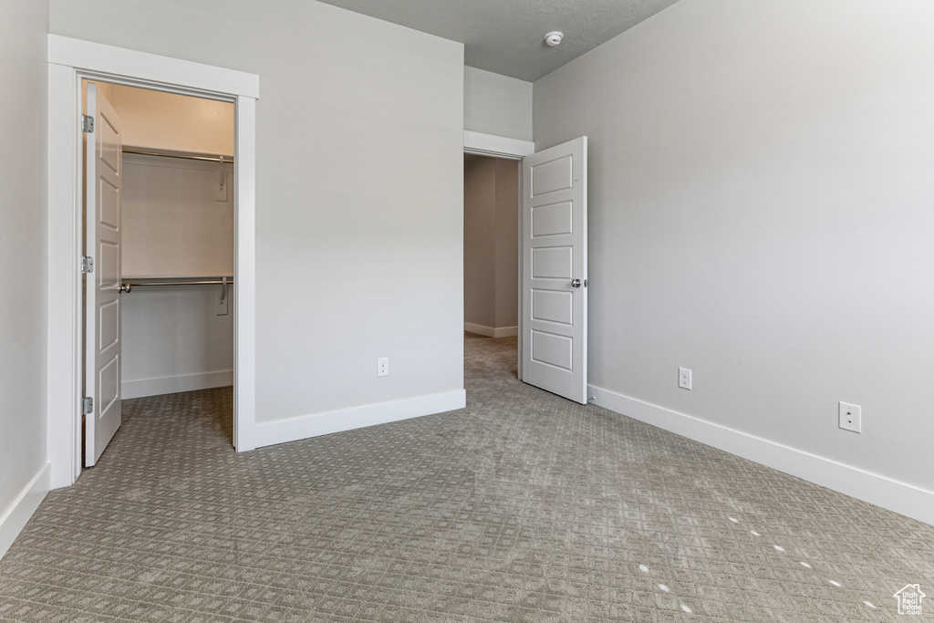 Unfurnished bedroom with carpet floors, baseboards, a walk in closet, and a closet