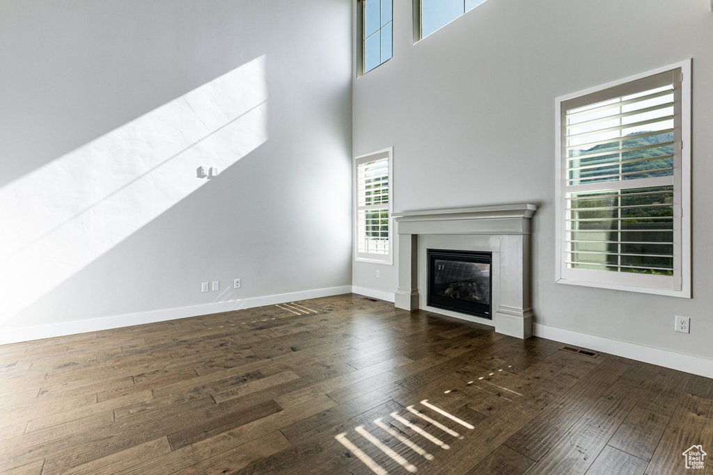 Unfurnished living room featuring a glass covered fireplace, hardwood / wood-style floors, baseboards, and a towering ceiling