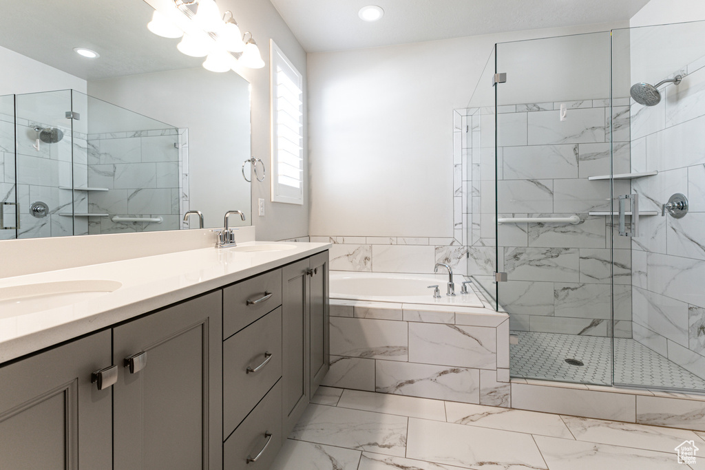 Bathroom featuring a bath, double vanity, a stall shower, marble look tiles, and recessed lighting