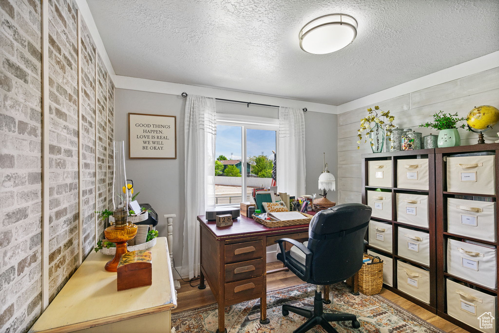Home office featuring a textured ceiling, brick wall, and wood finished floors