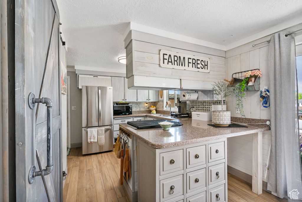 Kitchen featuring appliances with stainless steel finishes, a sink, light wood finished floors, backsplash, and light stone counters