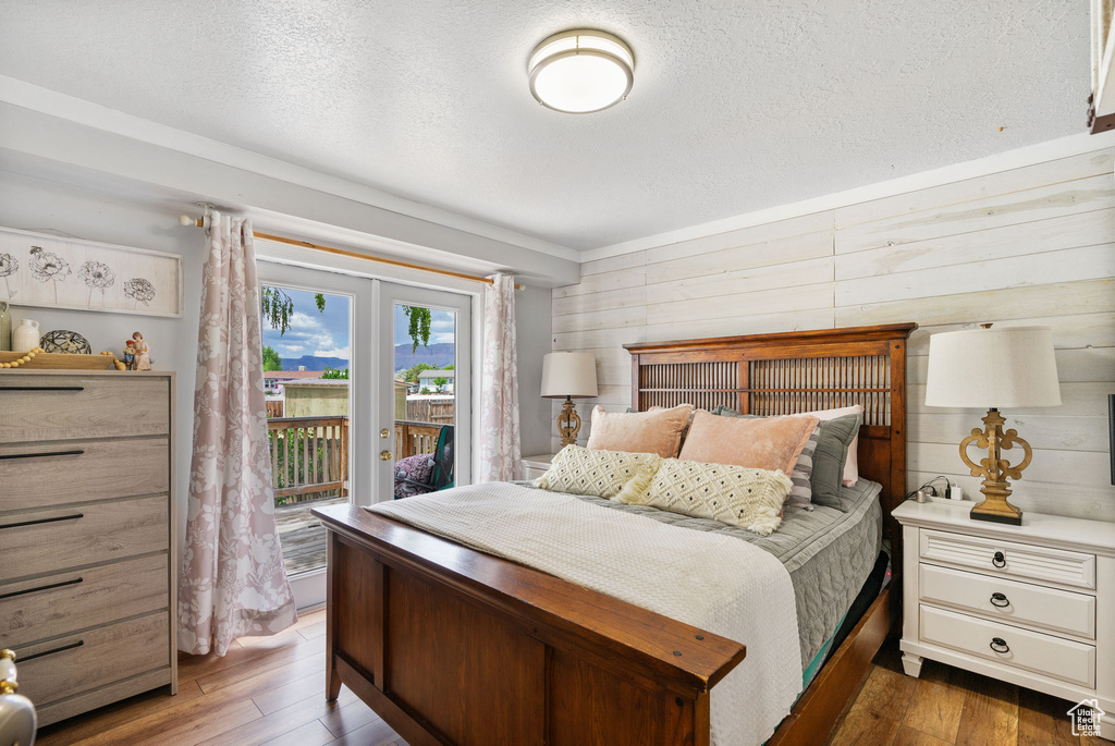 Bedroom featuring access to exterior, wood finished floors, a textured ceiling, and wood walls
