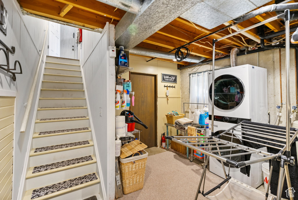 Basement with stacked washing machine and dryer, stairs, and carpet floors