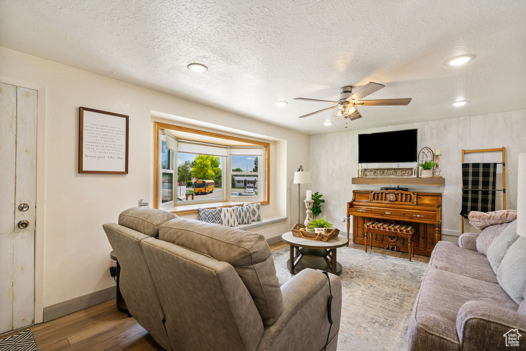 Living area with a ceiling fan, wood finished floors, baseboards, a textured ceiling, and recessed lighting