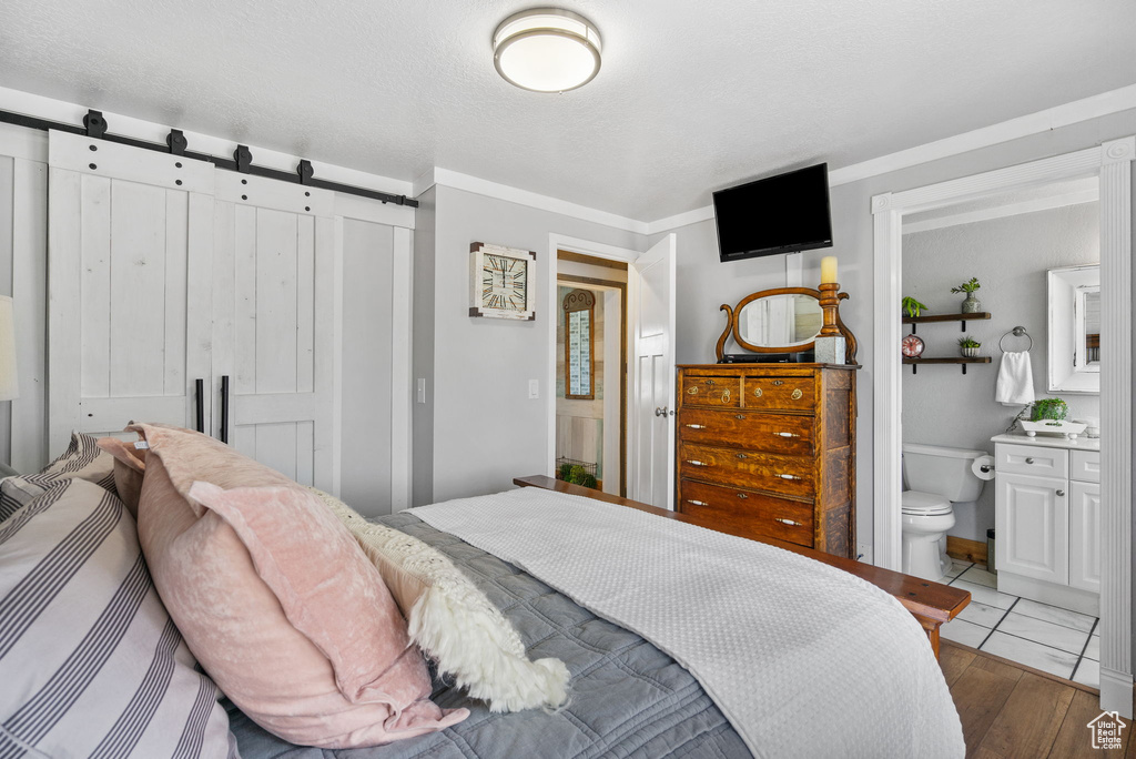 Bedroom featuring a barn door, a closet, wood finished floors, ensuite bathroom, and ornamental molding