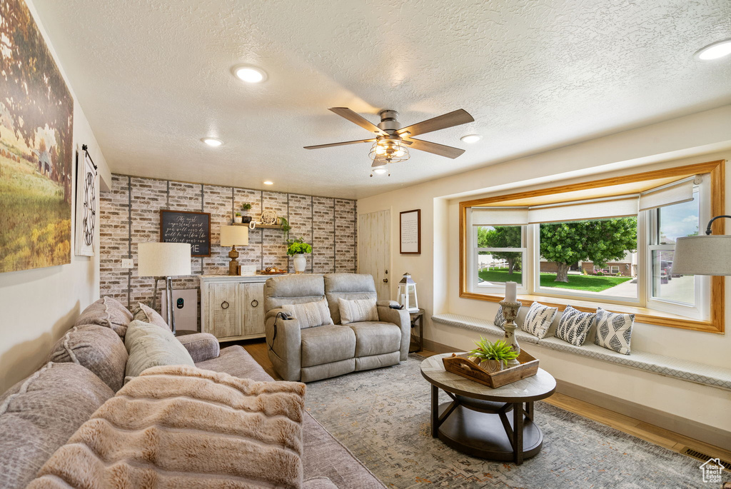 Living area featuring a textured ceiling, wood finished floors, a ceiling fan, brick wall, and recessed lighting