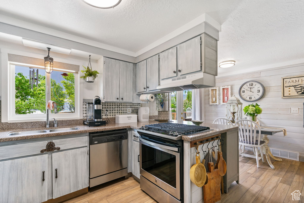 Kitchen with appliances with stainless steel finishes, a sink, a textured ceiling, light wood-style flooring, and under cabinet range hood