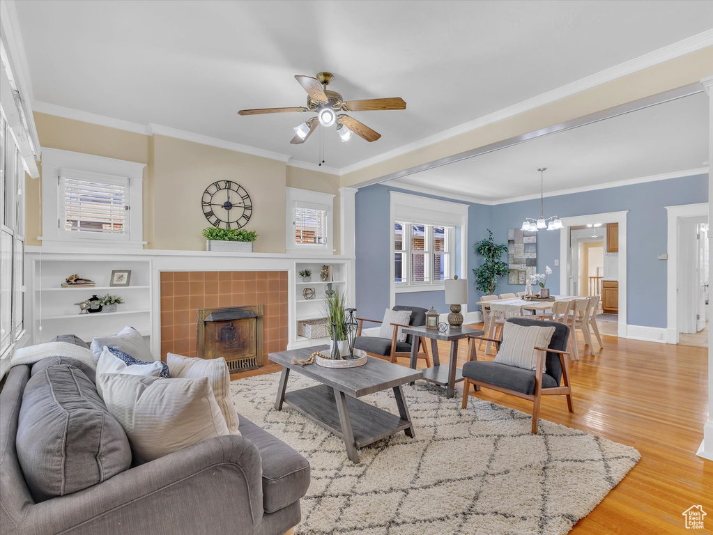 Living area featuring ceiling fan, a tiled fireplace, light wood-type flooring, plenty of natural light, and crown molding