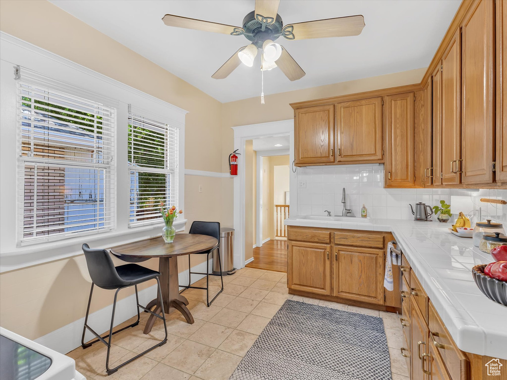 Kitchen with tile counters, a sink, decorative backsplash, light tile patterned floors, and ceiling fan