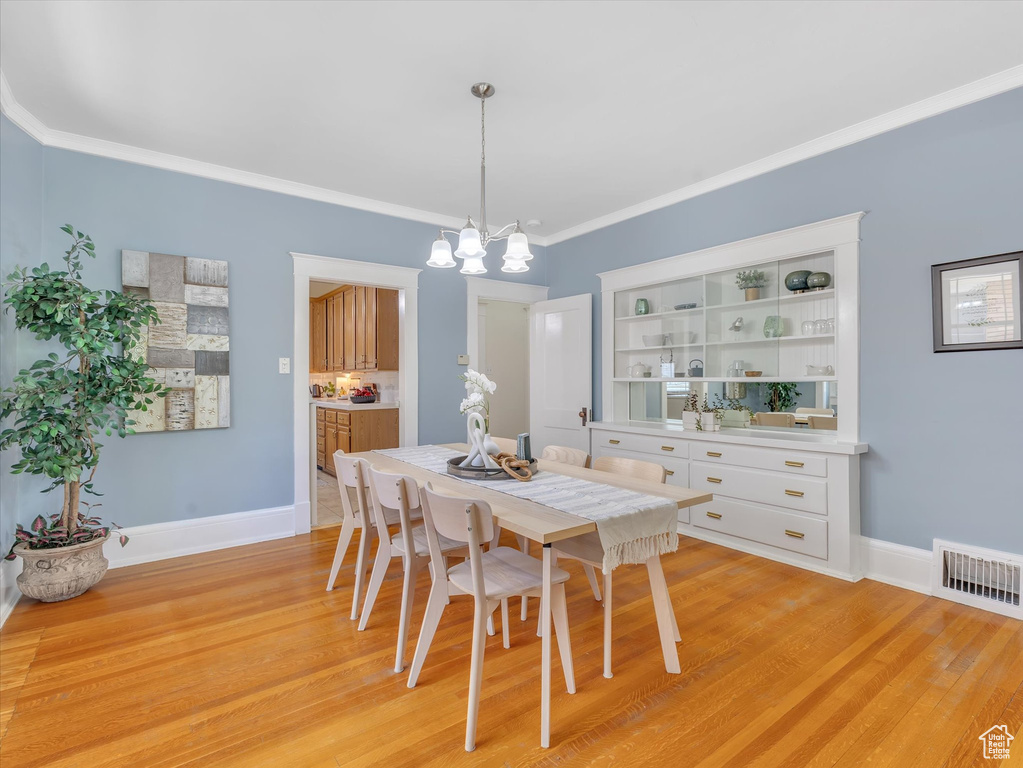 Dining area with a chandelier, light wood-type flooring, crown molding, and baseboards