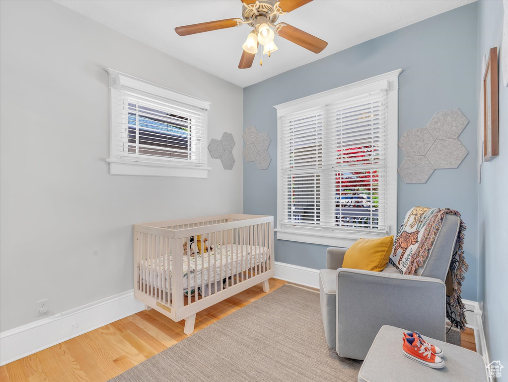 Bedroom featuring wood finished floors, a crib, baseboards, and ceiling fan