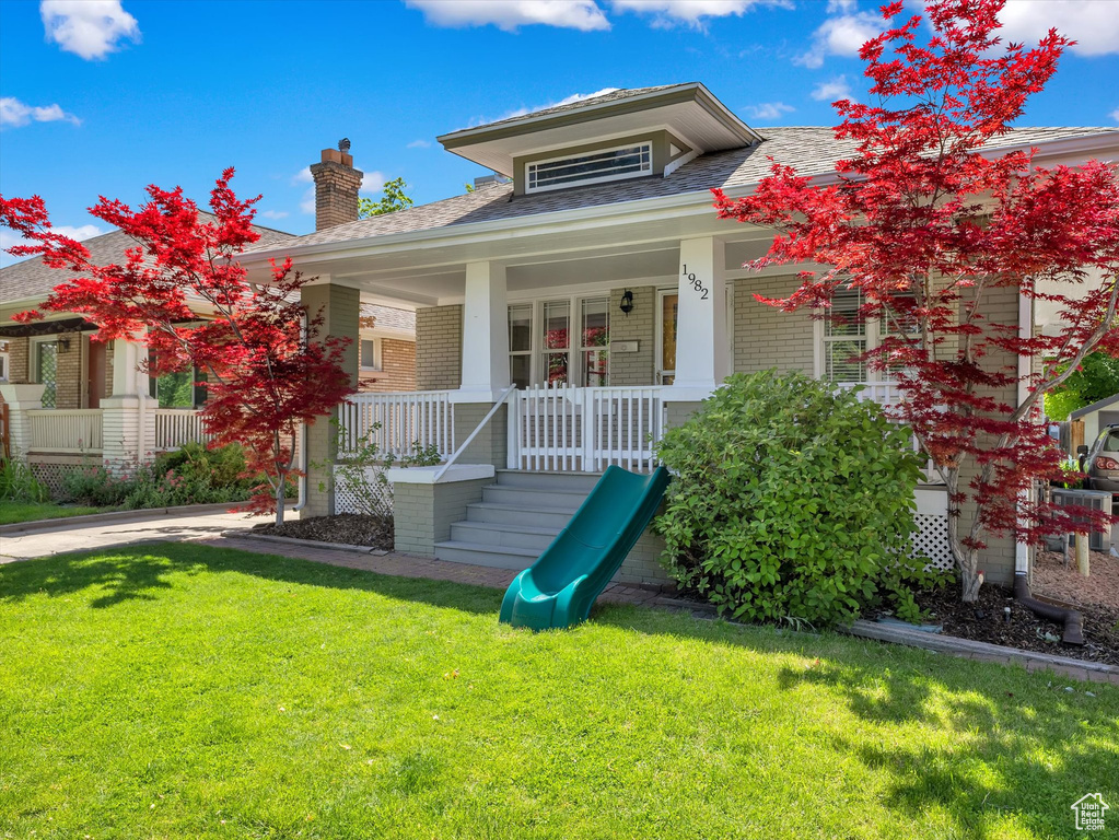 Bungalow-style home with brick siding, a front lawn, a chimney, and a porch