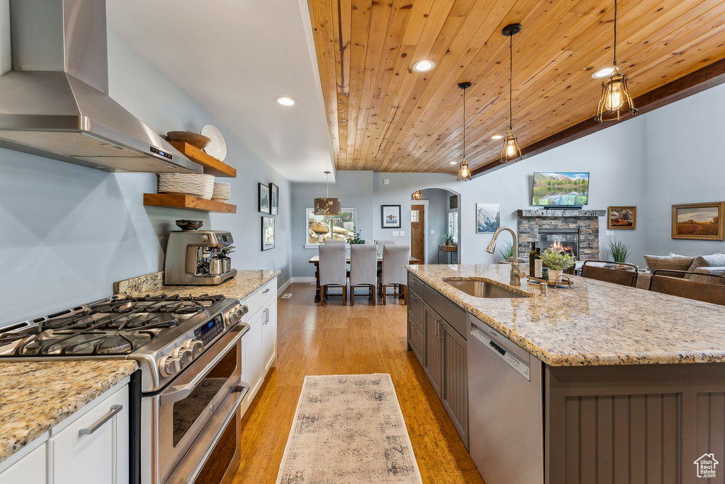 Kitchen with stainless steel appliances, island exhaust hood, a sink, arched walkways, and wooden ceiling