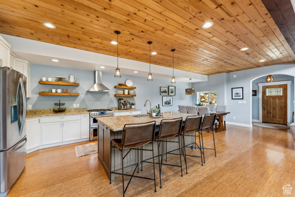 Kitchen featuring stainless steel appliances, wall chimney exhaust hood, a sink, open shelves, and arched walkways