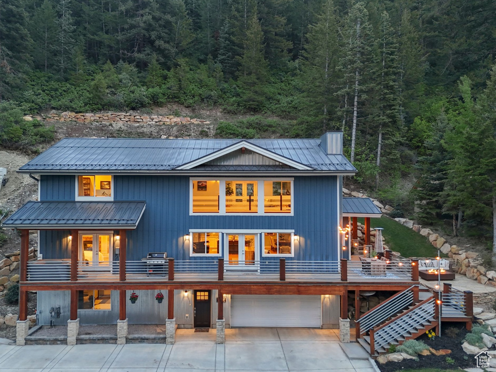 Back of house with a view of trees, covered porch, a garage, and metal roof