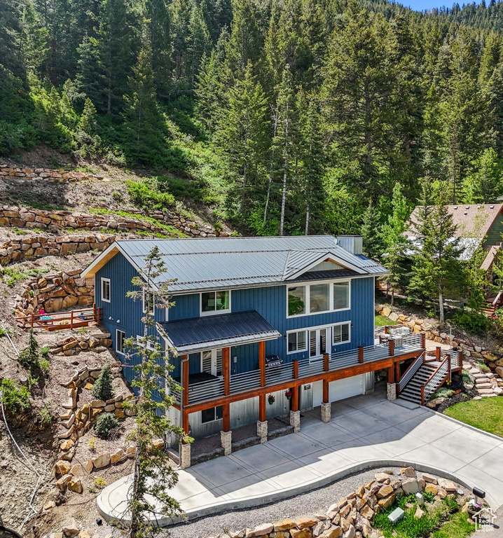 Rustic home with a wooded view, concrete driveway, metal roof, stairway, and a garage