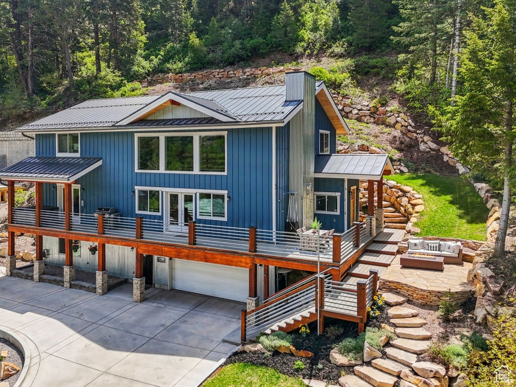 View of front facade featuring metal roof, an outdoor fire pit, driveway, an attached garage, and a wooden deck