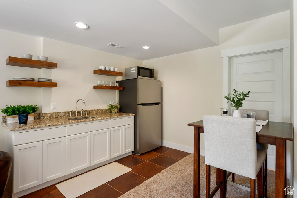 Kitchen featuring a sink, freestanding refrigerator, open shelves, light stone countertops, and recessed lighting