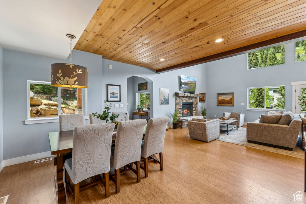 Dining room with arched walkways, a stone fireplace, light wood-style floors, wooden ceiling, and recessed lighting