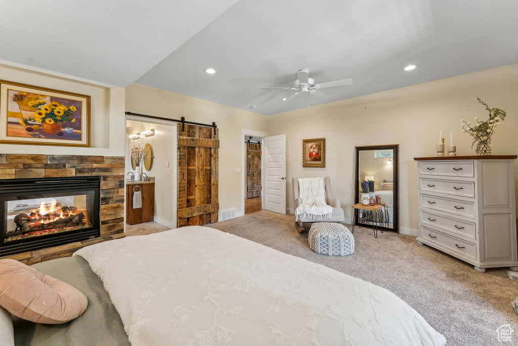 Bedroom with a barn door, light colored carpet, recessed lighting, baseboards, and a stone fireplace