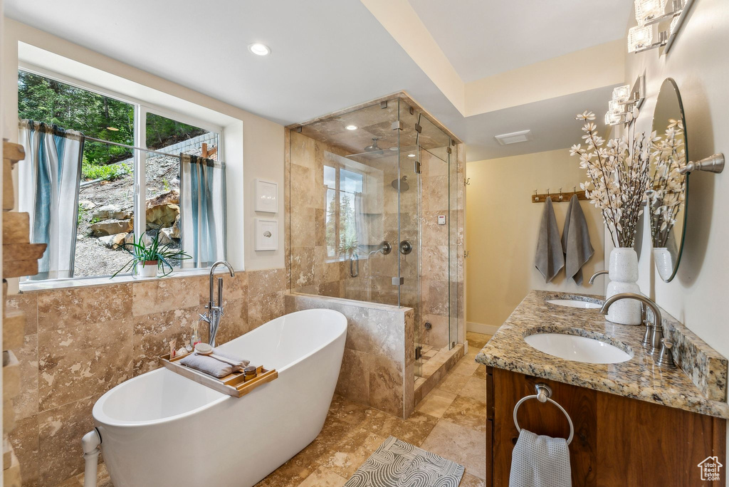 Bathroom featuring a shower stall, a freestanding bath, tile walls, double vanity, and recessed lighting
