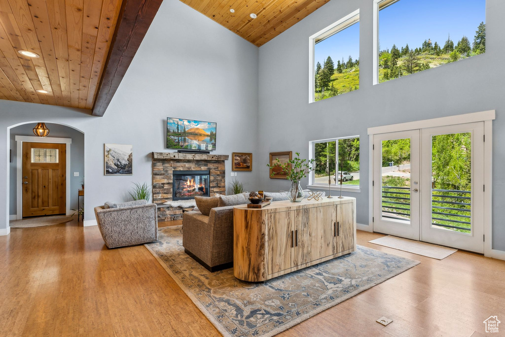 Living area with wooden ceiling, high vaulted ceiling, wood finished floors, a stone fireplace, and arched walkways