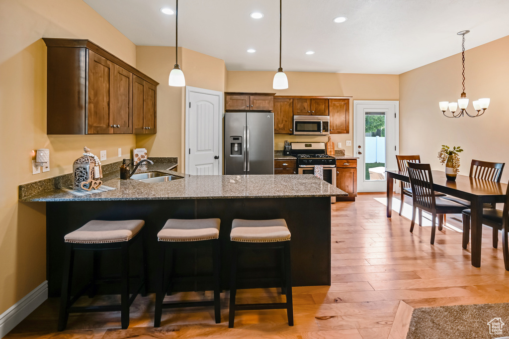 Kitchen with stainless steel appliances, a sink, a peninsula, light wood finished floors, and pendant lighting