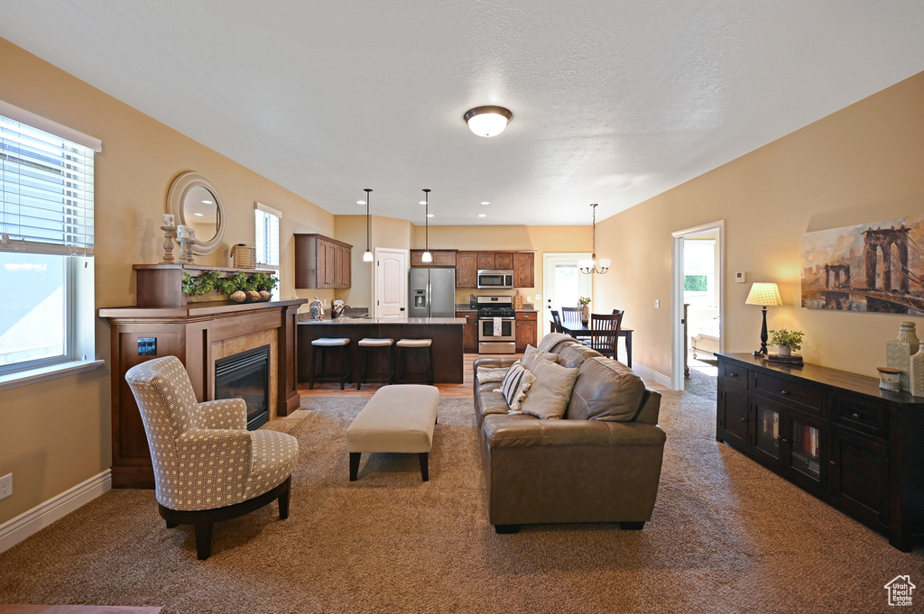 Carpeted living room featuring a glass covered fireplace, baseboards, and a chandelier