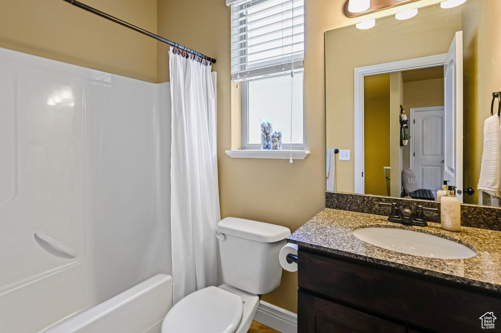 Full bathroom featuring toilet, vanity, shower / tub combo, and baseboards