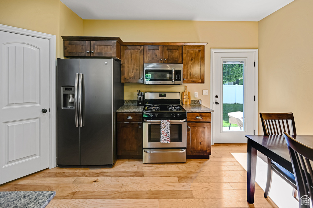 Kitchen featuring stainless steel appliances, light wood-style flooring, dark stone countertops, and dark brown cabinets