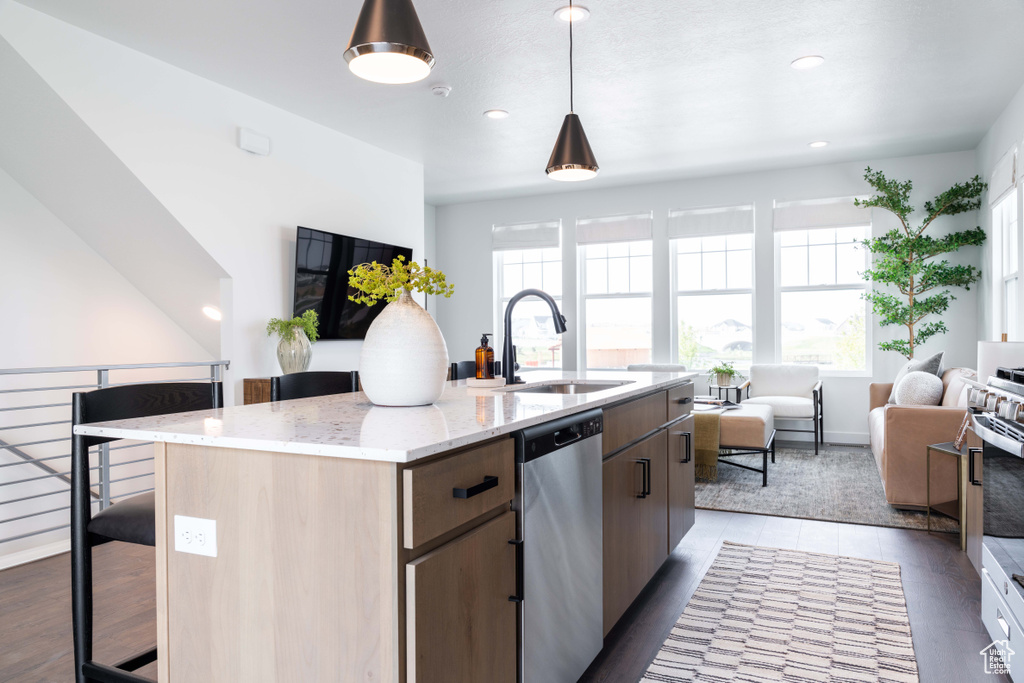 Kitchen with a sink, stainless steel appliances, open floor plan, a kitchen island with sink, and light stone countertops