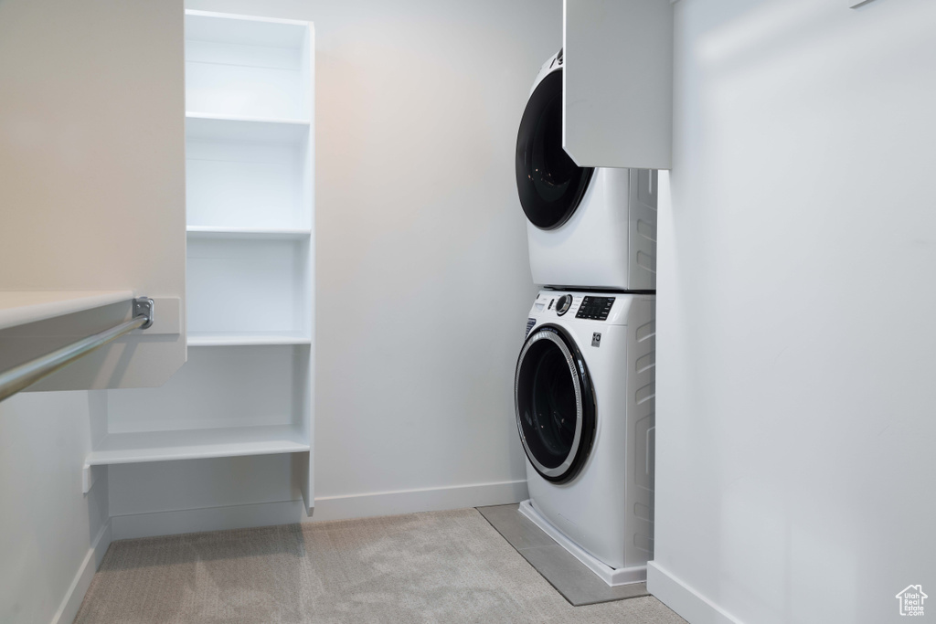 Laundry area featuring stacked washer and clothes dryer, light colored carpet, and baseboards
