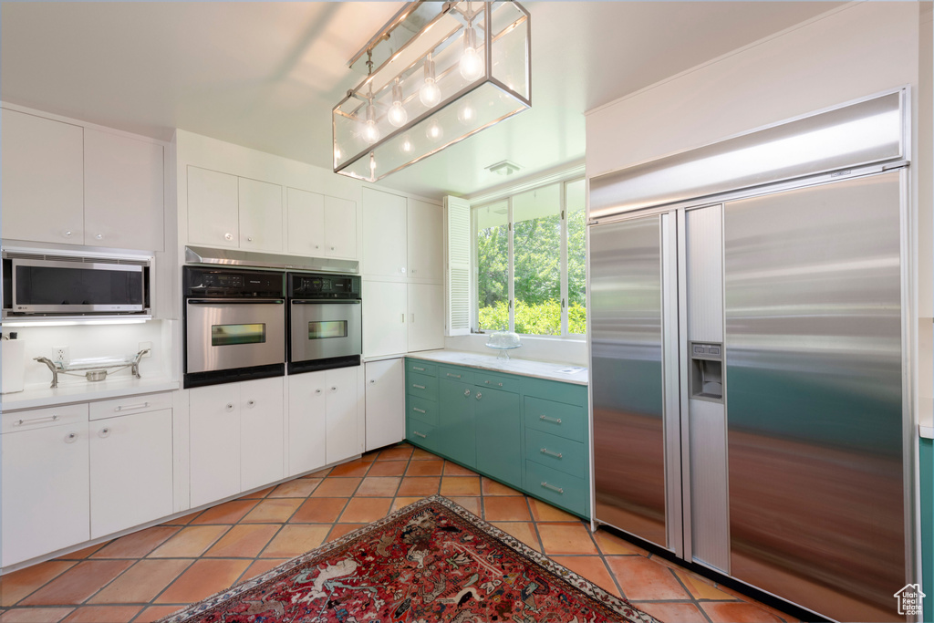 Kitchen featuring stainless steel appliances, white cabinetry, light tile patterned floors, and light countertops