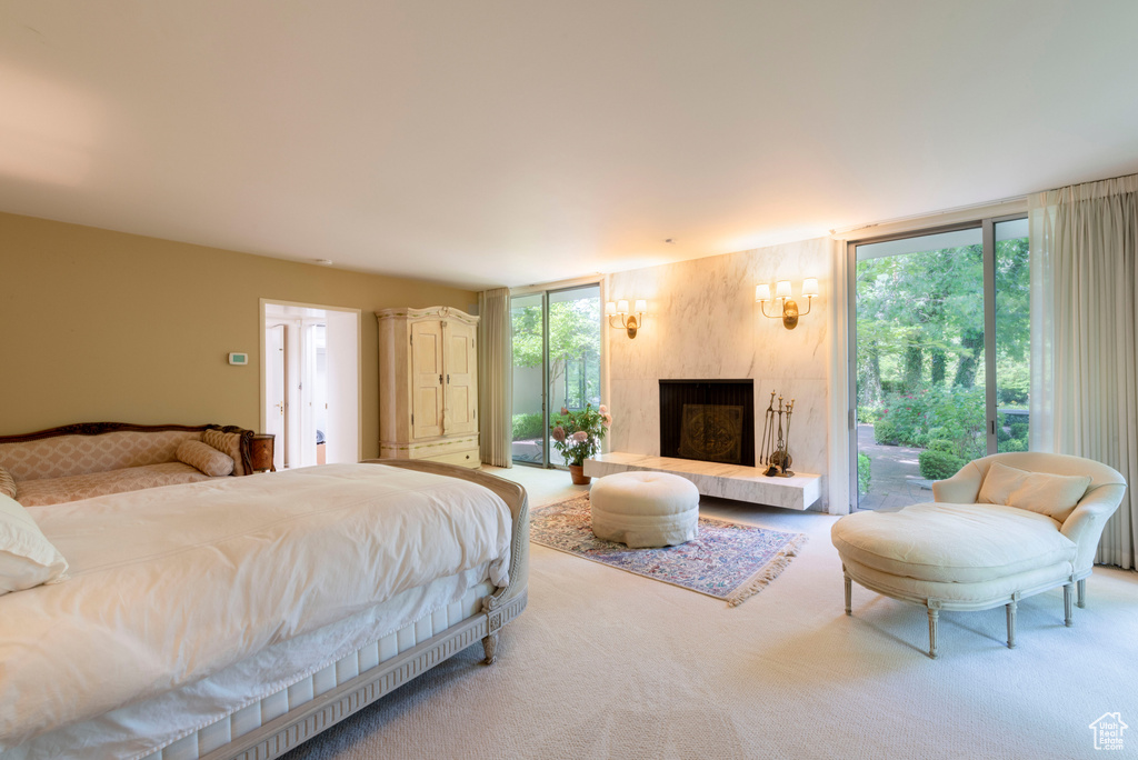 Bedroom with carpet flooring, access to exterior, a fireplace with raised hearth, and floor to ceiling windows