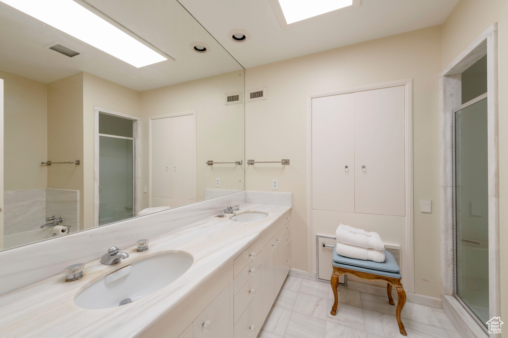 Full bathroom featuring double vanity, a stall shower, and baseboards