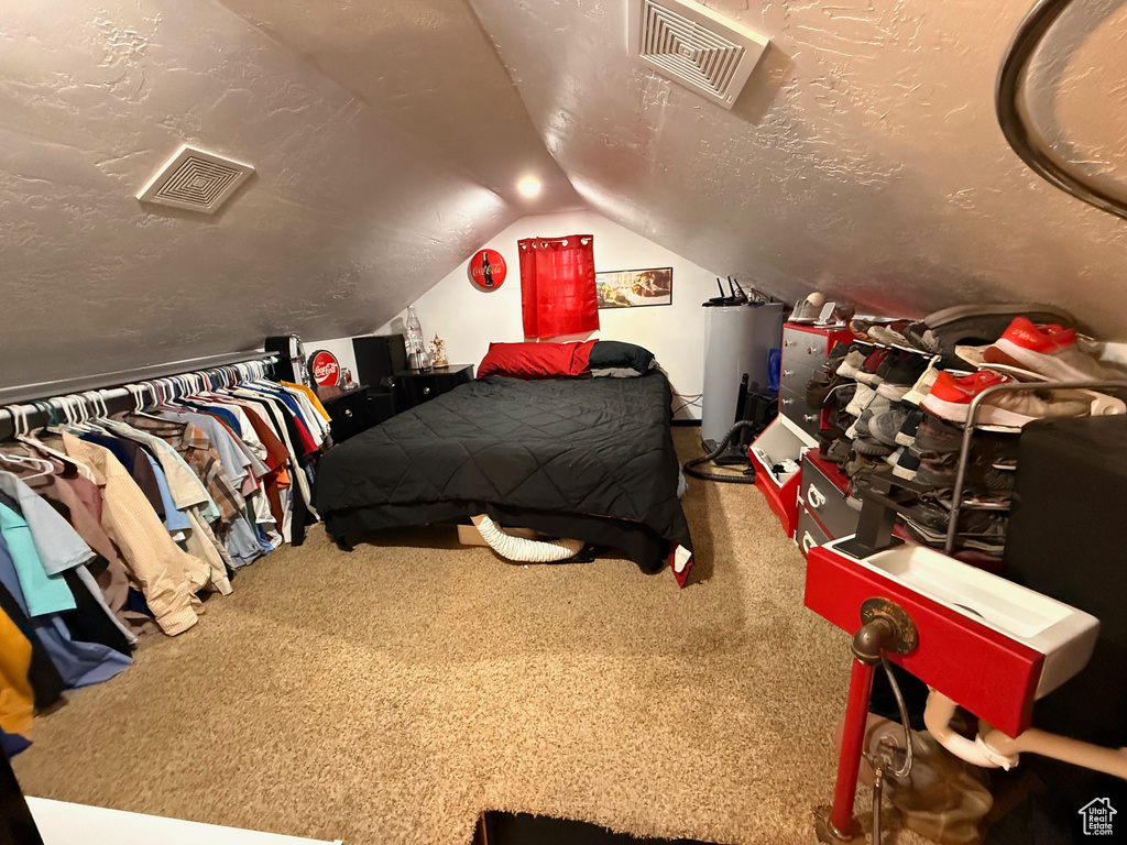 Carpeted bedroom featuring gas water heater, vaulted ceiling, and a textured ceiling